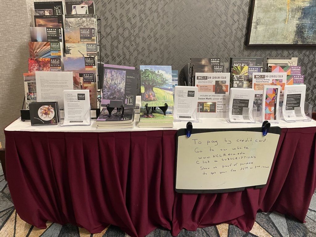 copies of North Carolina Literary Review stacked on a table, which is draped with a burgandy tablecloth