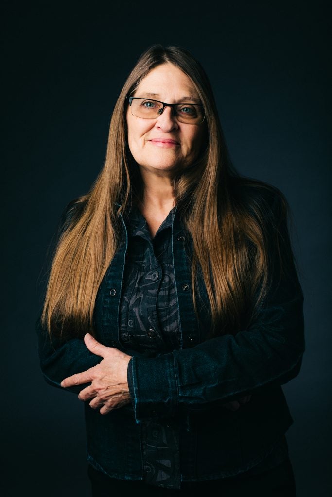 Hedge Coke, wearing long brunette hair, black shirt and jacket, with glasses on