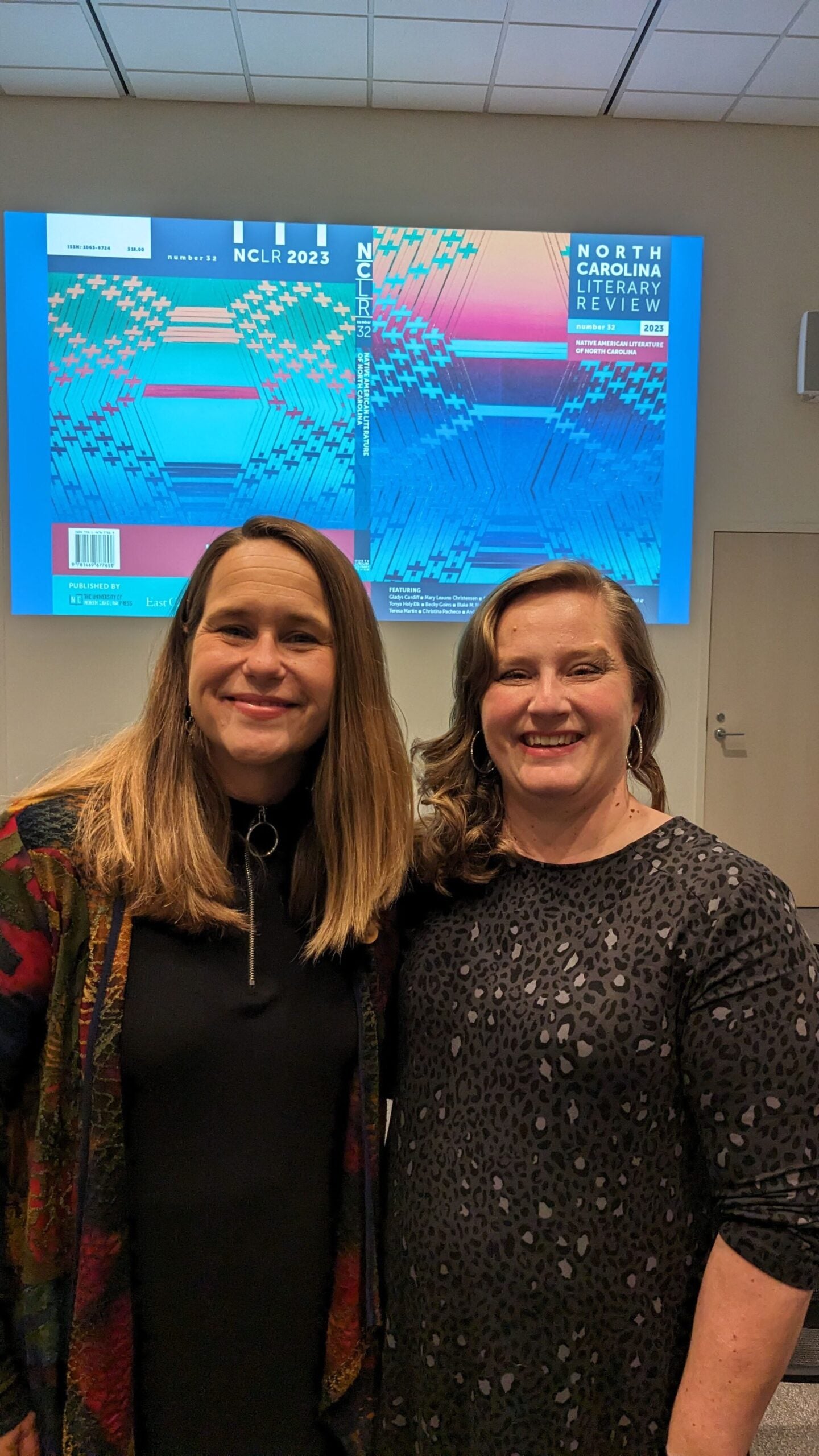 two white women with blonde hair in front of a screen with the 2023 issue of NCLR projected on it