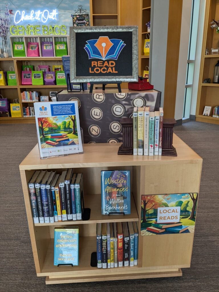 "read local" sign on a library display of books by North Carolina authors. Three shelves hold almost two dozen books. 